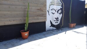 Un mur orné d’une fresque, deux cactus en pot et une clôture en bois.
