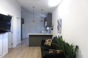 Eine moderne Küche mit Kochinsel, einem Essbereich mit schwarzem Sofa und einem an der Wand befestigten Flachbildfernseher.