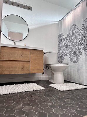Een badkamer met een houten wastafelmeubel, toilet, spiegel en een douchegordijn met zwart-wit patroon.