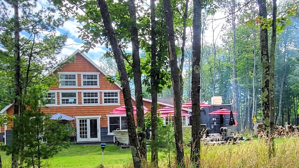 A two-story house with a red roof, surrounded by trees and a grassy yard.