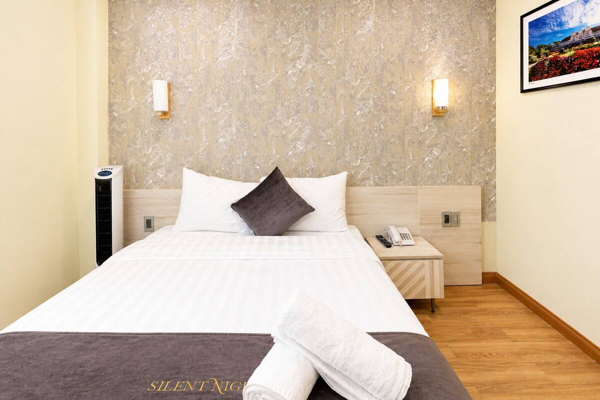 A hotel room with a bed, a nightstand, a phone, and a wall-mounted light fixture.