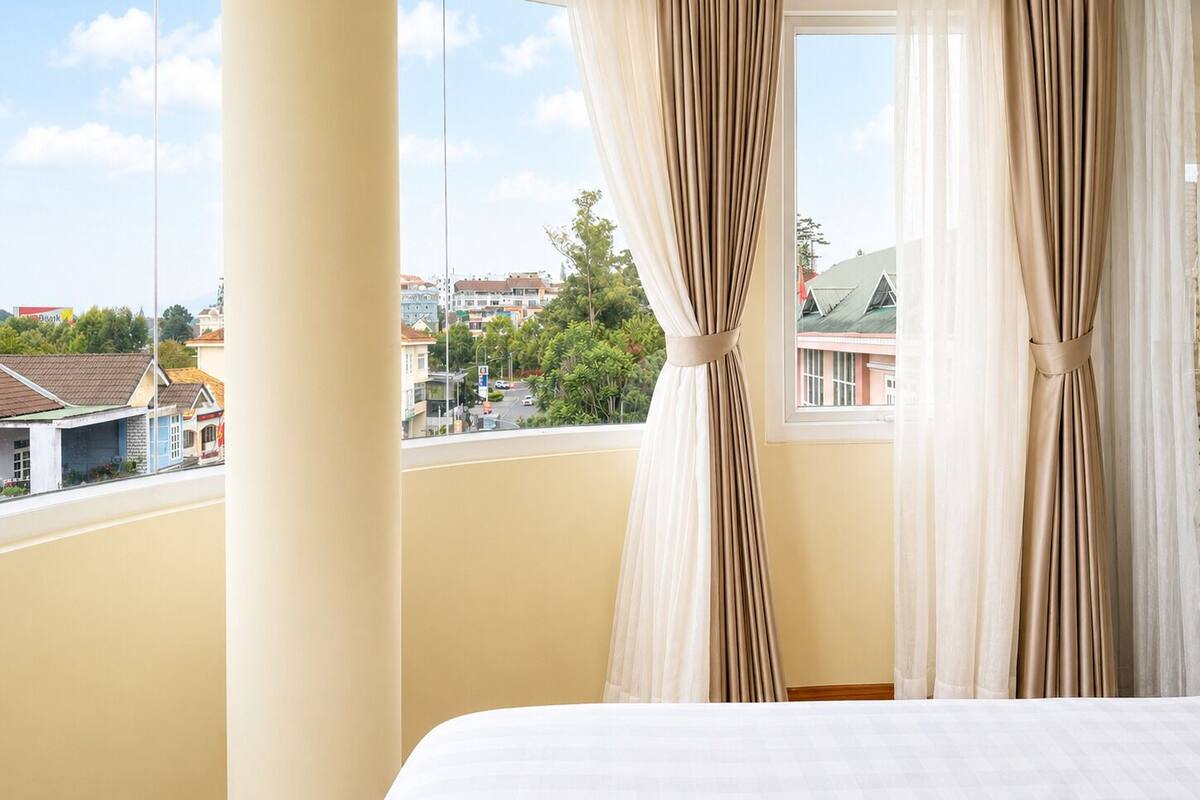 A hotel room with a large window, curtains, and a view of the cityscape.