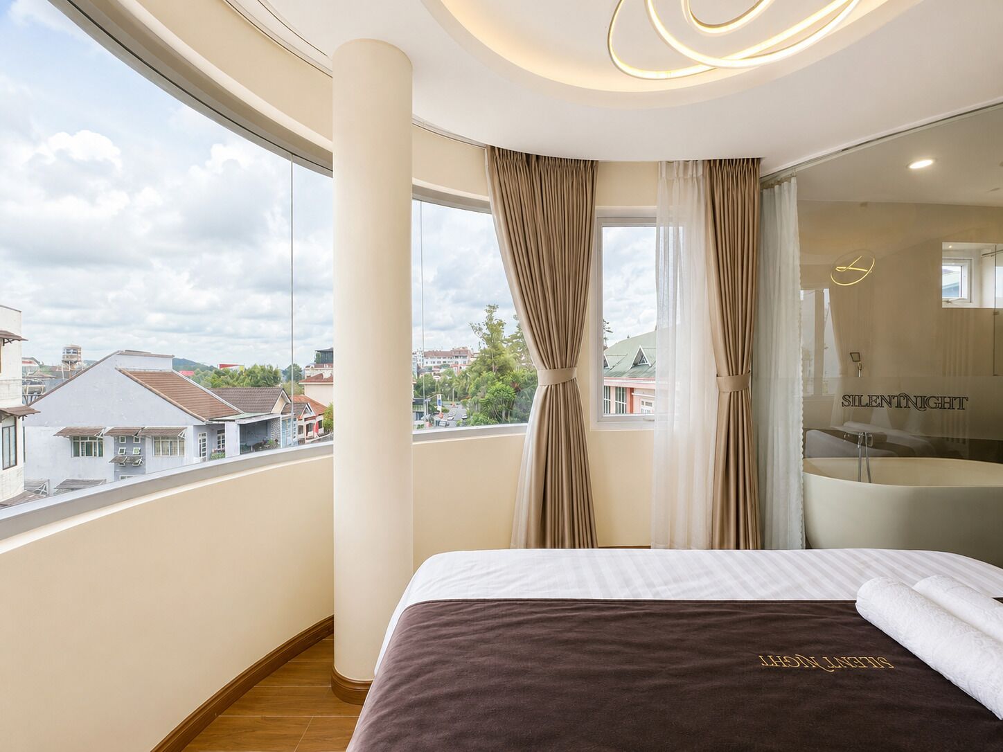 A hotel room with a large bed, a bathroom with a bathtub, and a balcony with a view of the city.