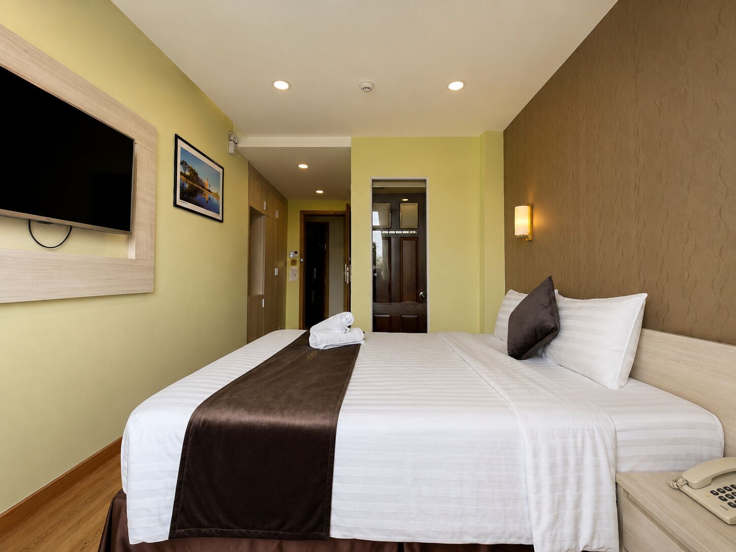 A hotel room with a bed, a bedside telephone, a television mounted on the wall, and a door leading to a bathroom.