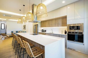 Une cuisine moderne dotée d’un îlot central, de tabourets de bar, de luminaires suspendus et d’appareils électroménagers intégrés.