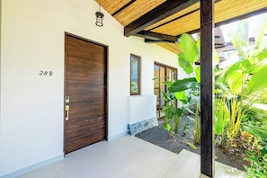 A modern entrance with a wooden door, a number '28B' on the wall, and a covered area with plants. - Charming Villa with Pool, Modern Amenities & Near Famous Surf Spots (Tamarindo)