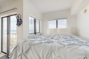 A bedroom with a large bed, two windows, a door leading to a balcony, and a ceiling light fixture. - Oceanfront studio with private balcony, pool & direct beach access (Myrtle Beach)
