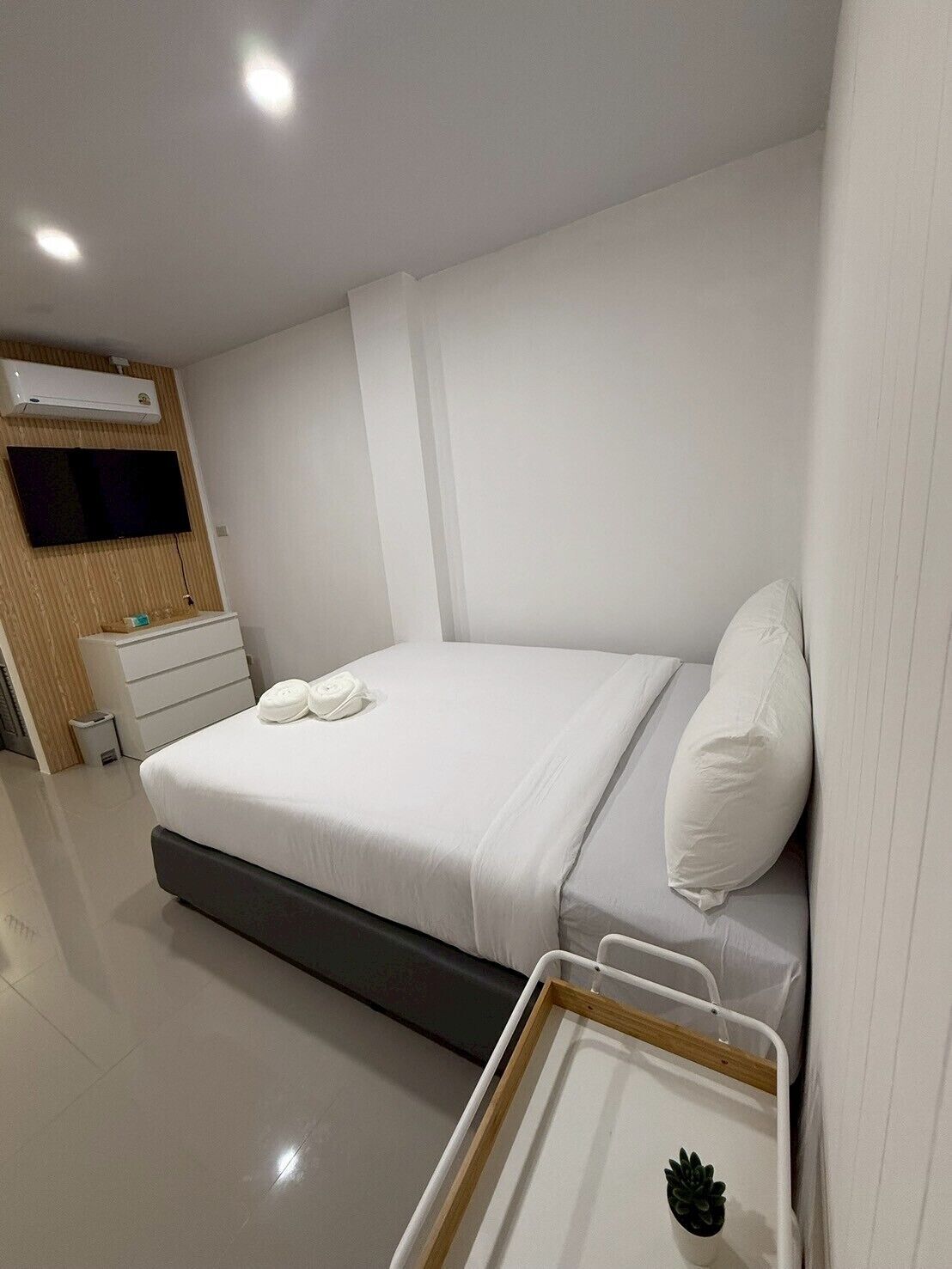 A modern hotel room with a bed, a bedside table, a TV, and an air conditioning unit.