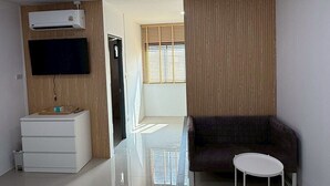 A modern hotel room with a flat-screen TV, a sofa, a small round table, and a bed. - I Am Daily Mansion (Pluak Daeng)