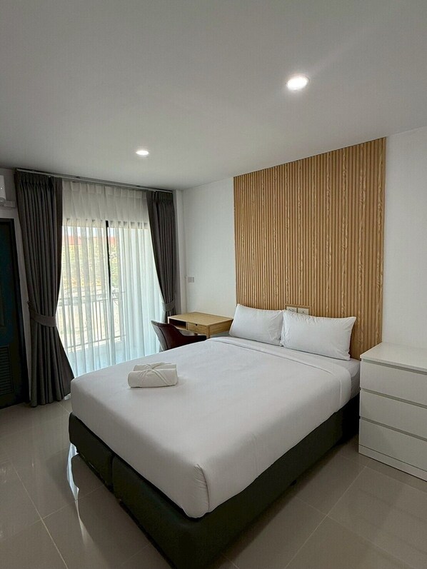A modern hotel room with a large bed, a wooden headboard, a desk, and a view through the window. - I Am Daily Mansion (Pluak Daeng)