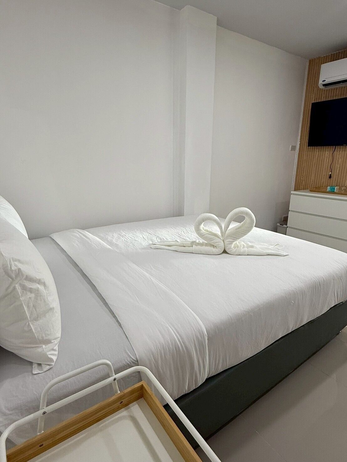 Una camera d'albergo con un letto rifatto, un comodino, una TV fissata al muro e un pannello in legno sopra la TV.