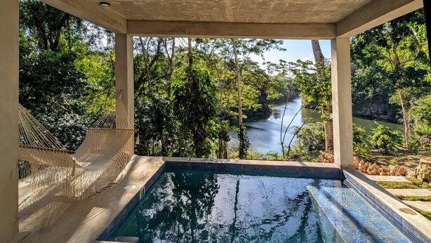 Una piscina con una hamaca, rodeada de exuberante vegetación y vistas al río.