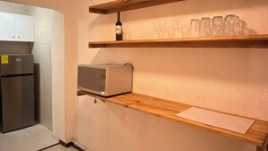 A kitchen with a refrigerator, microwave, and wooden shelves with glasses and a bottle. - Encantador depa en Polanco, Ideal para viajeros. (Ciudad de México)