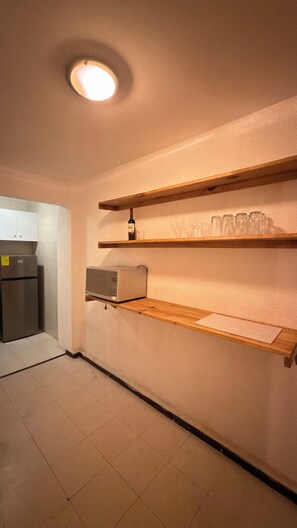 Eine Küche mit Kühlschrank, Mikrowelle und Holzregalen mit Gläsern und einer Flasche.