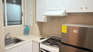 A compact kitchen with white cabinets, a stainless steel stove, a refrigerator, and a window with a view. - Encantador depa en Polanco, Ideal para viajeros. (Ciudad de México)