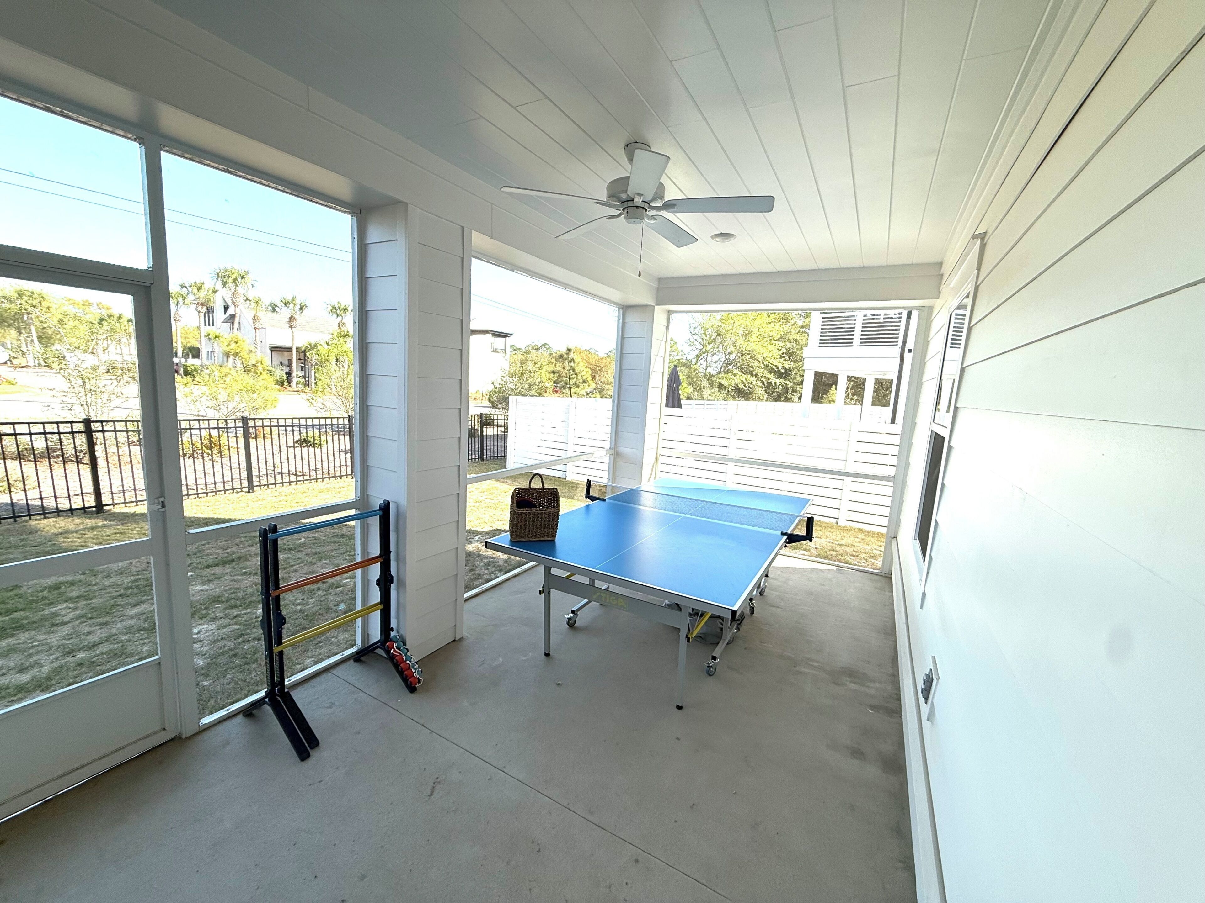Un patio techado con mesa de ping pong, ventilador de techo y un estante con equipo de ejercicio.
