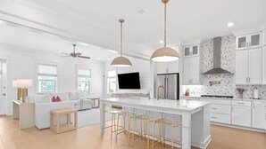 Une cuisine moderne dotée d’un îlot central, de tabourets de bar, de luminaires suspendus et de meubles blancs.