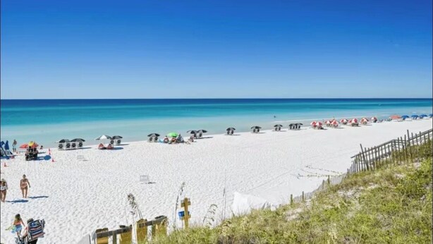 Une plage de sable blanc, avec une eau d’un bleu limpide et plusieurs parasols de plage.