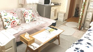 Une pièce confortable avec un canapé, un petit bureau, un four à micro-ondes et une poubelle.