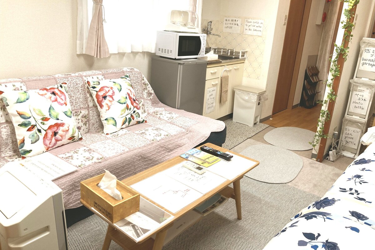 A cozy room with a sofa, a small desk, a microwave, and a trash bin.