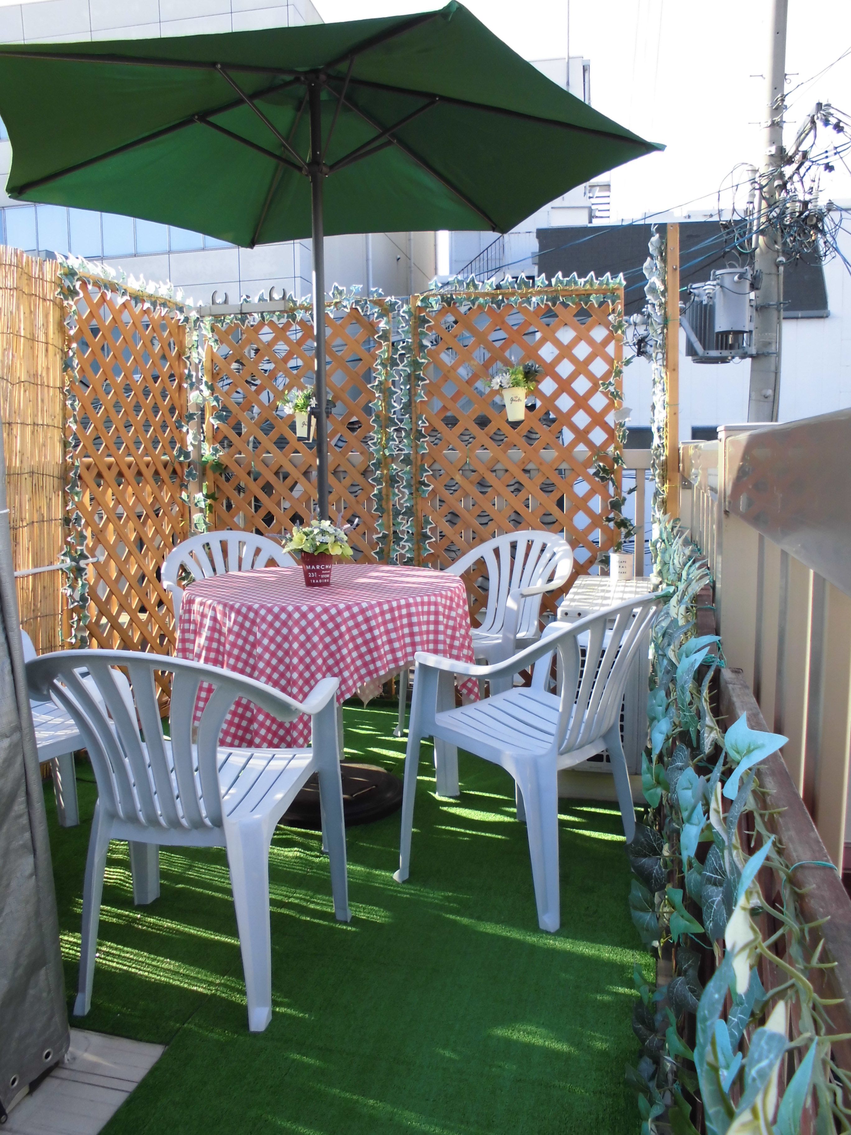 Un patio exterior con una mesa, sillas, un paraguas verde y una valla de madera con plantas.