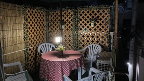 Un espace de restauration en plein air avec une table et des chaises, une nappe à motifs et un mur en treillis orné de plantes grimpantes.