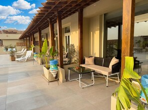 A covered outdoor seating area with lounge chairs and tables, surrounded by potted plants. - Pyramids Khan Hotel (Giza)