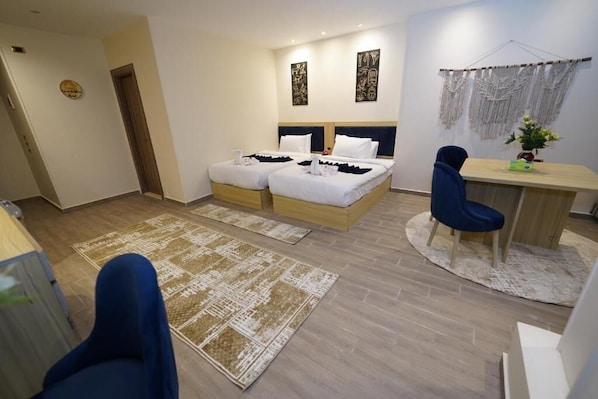 A hotel room with two beds, a desk, a chair, and a small desk lamp.