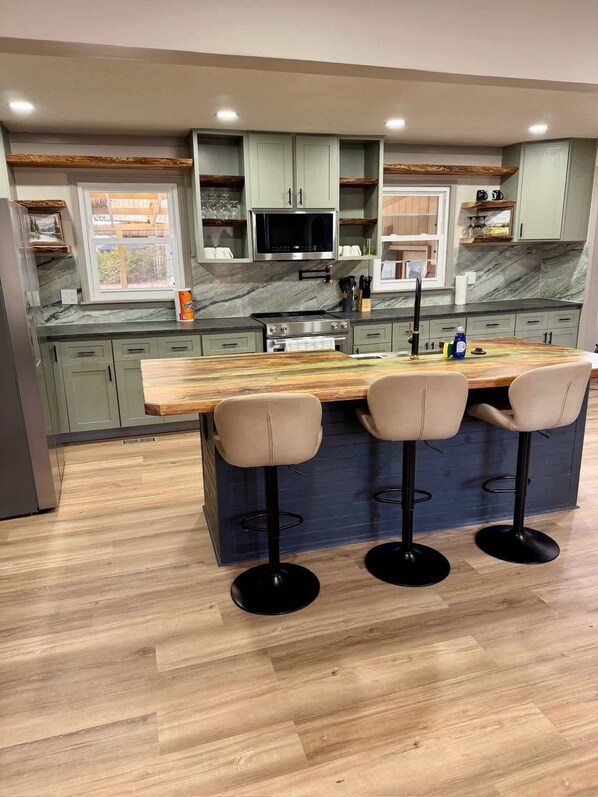 A modern kitchen with a central island, bar stools, and a microwave.