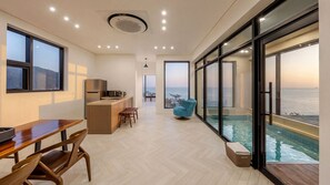 A modern kitchen with a view of the sea, a dining area with a wooden table, and a large window overlooking a swimming pool. - Pohang Sausalito by B-class Pool Villa (Pohang)