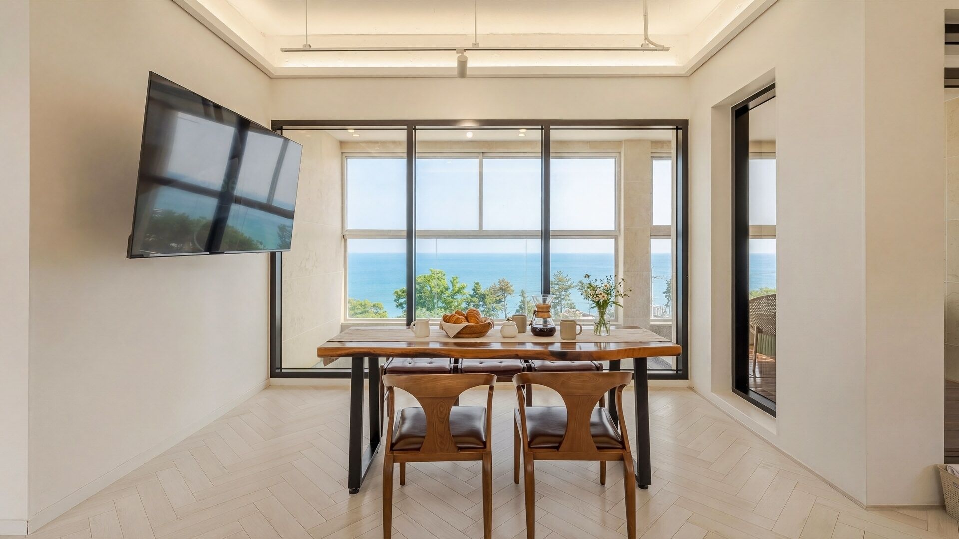 A dining area with a table, chairs, a TV, and a view of the sea.