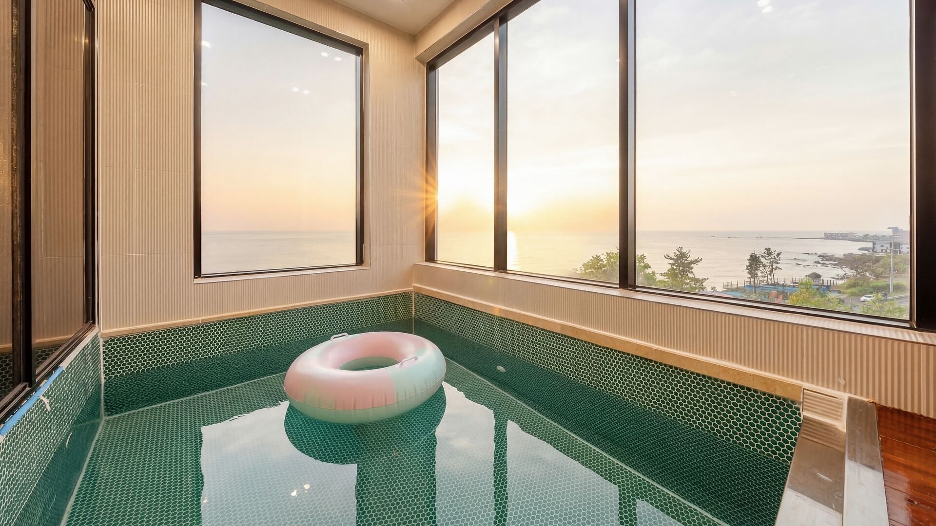 A room with a large window overlooking a body of water, a floating ring, and a tiled floor.