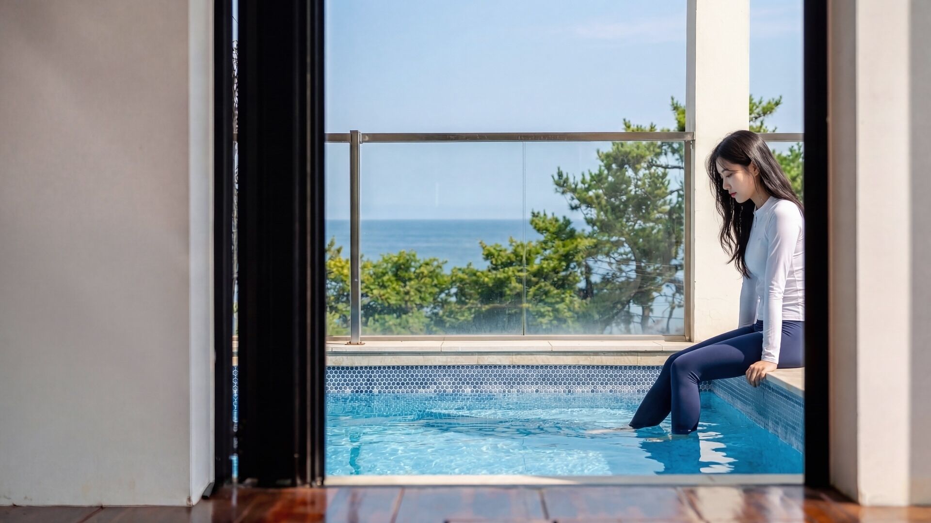 A person sitting by a window overlooking a swimming pool.