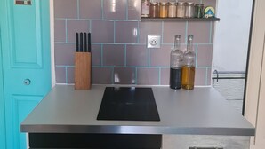 Eine Küche mit einer Edelstahl-Dunstabzugshaube, einem schwarzen Induktionskochfeld, einem Geschirrspüler und einem grauen Schrank mit weißem Griff.