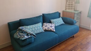 Ein senffarbenes Sofa mit gemusterten Kissen, ein kleiner weißer Schrank und eine Wandlampe.