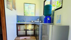 Une cuisine compacte équipée d’un évier, d’un réfrigérateur et d’une fenêtre donnant sur un espace verdoyant.