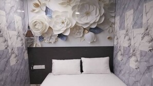 A hotel room with a bed, white pillows, a brown blanket, and a wall with large floral decorations. - Port Dickson Seafront Hotel (Port Dickson)