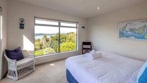 A bedroom with a large window, a bed, a wicker chair, and a map on the wall. - Wakainga — Church Bay Estate (Waiheke Island)