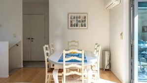A dining area with a round table, white chairs, a blue placemat, and a framed picture on the wall. - Wakainga — Church Bay Estate (Waiheke Island)