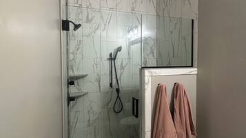 A bathroom with a glass-enclosed shower, marble walls, a toilet, and a towel rack.