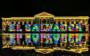 A building with illuminated letters spelling 'EL SALZON' on its facade, reflecting on water in front.