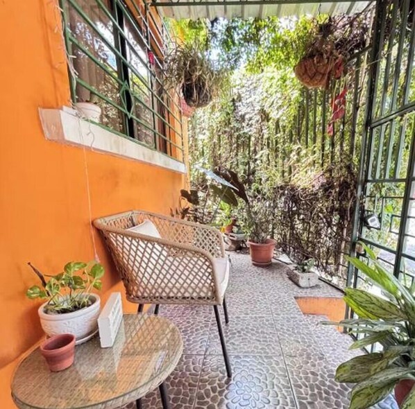 A covered outdoor area with a tiled floor, wicker furniture, and potted plants.