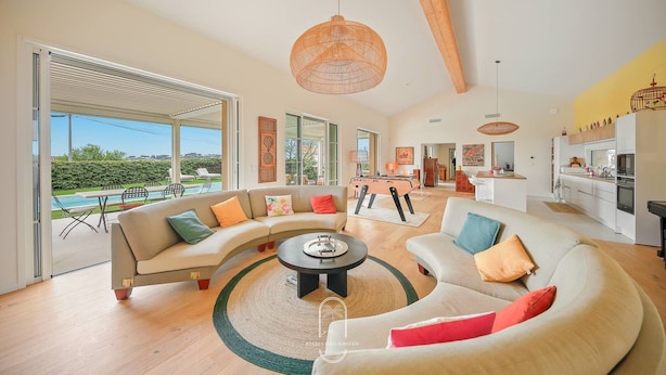 A spacious living area with a curved sofa, a round coffee table, and a view of a pool and garden. - Villa La Carqueiranaise (CARQUEIRANNE)