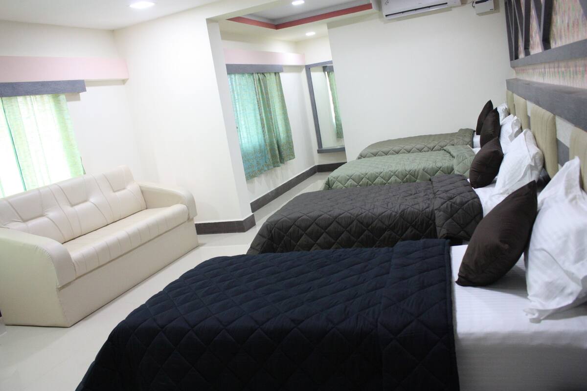 A hotel room with a sofa, two beds with quilts, a mirror, and a window with curtains.