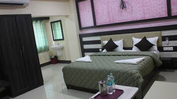 A hotel room with a bed, a bedside table with water bottles, a wardrobe, a sink, and a mirror.