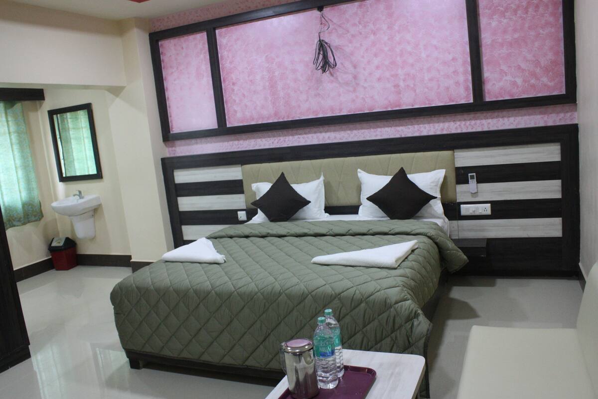 A hotel room with a bed, bedside table, and a wall-mounted sink.