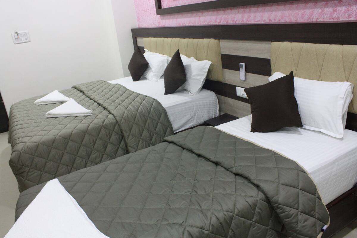 A hotel room with two beds, each with a quilted bedspread and pillows.