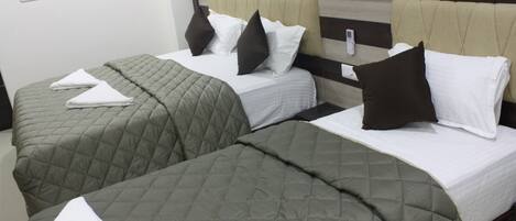 A hotel room with two beds, each with a quilted bedspread and pillows.