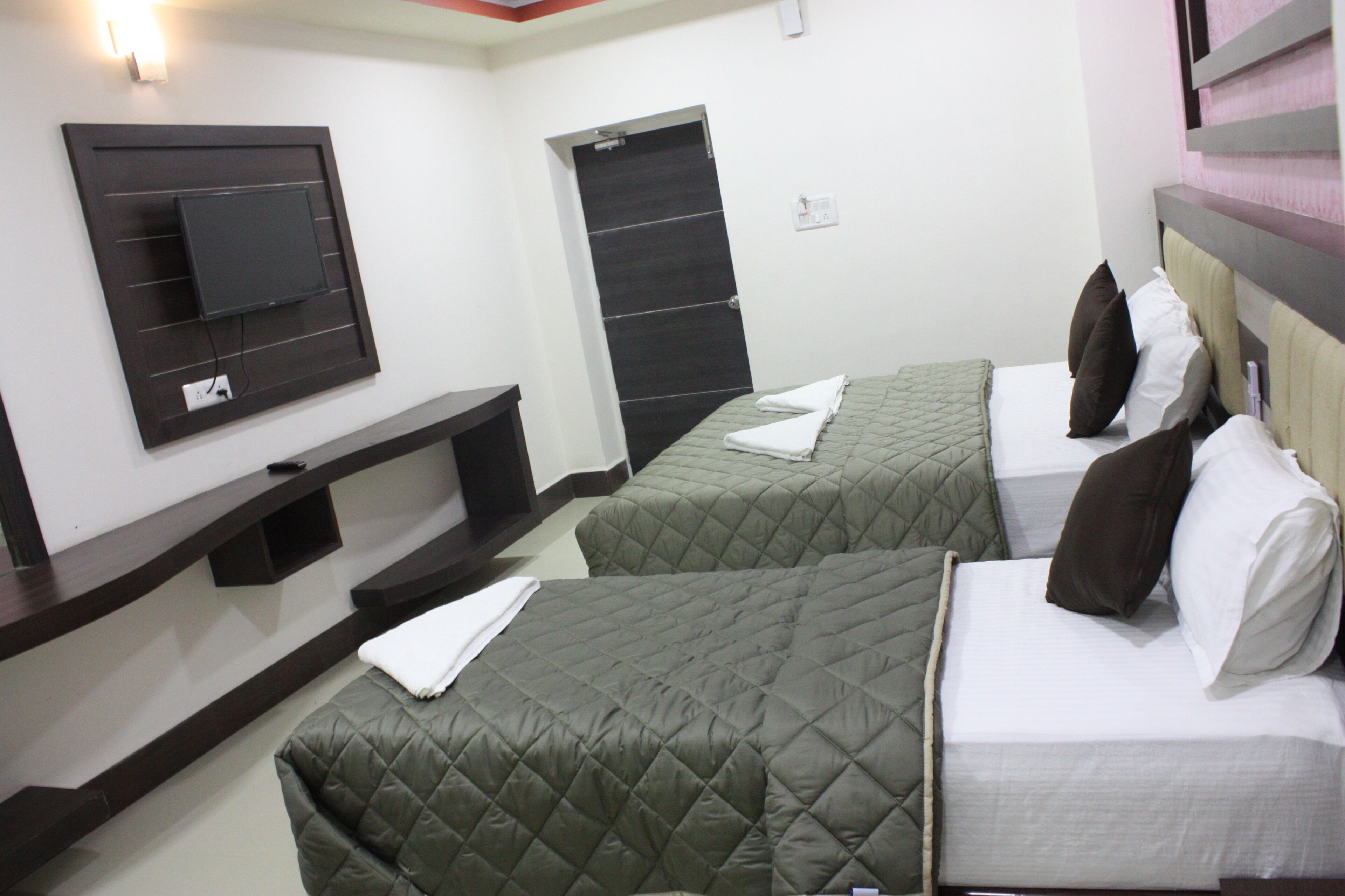 A hotel room with two beds, a flat-screen TV mounted on the wall, and a door.