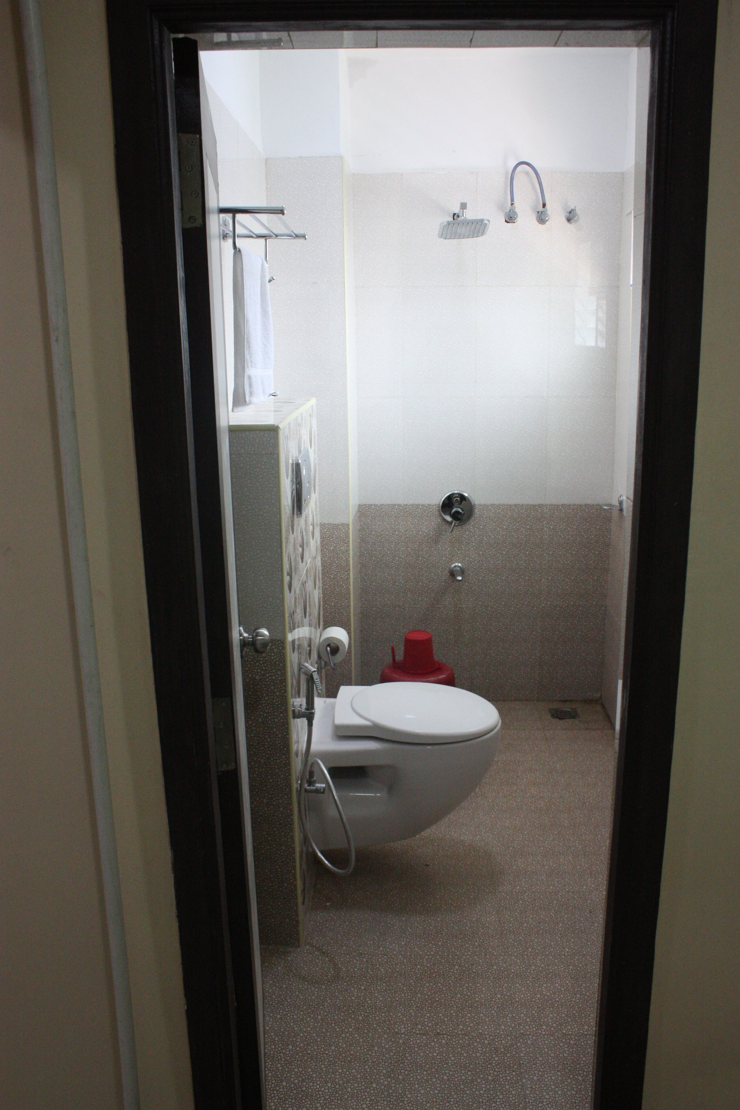 A small, enclosed bathroom with a toilet, a shower, and a towel rack.